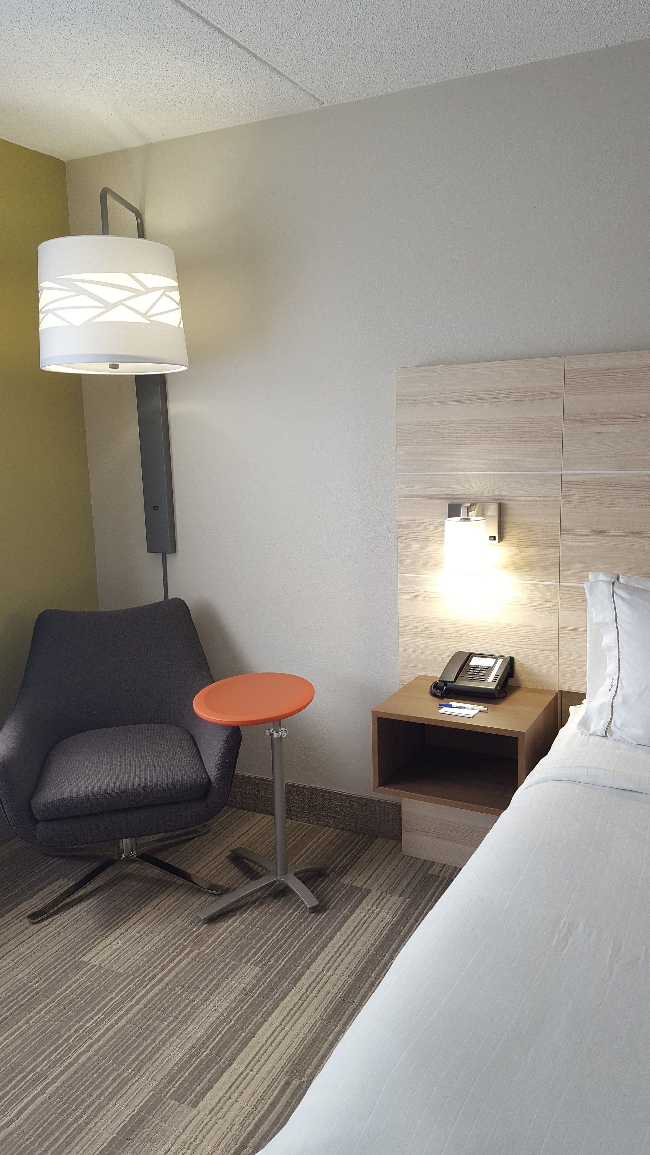 A hotel room with a bed, a desk with a phone, a chair, a small table, and a lamp.
