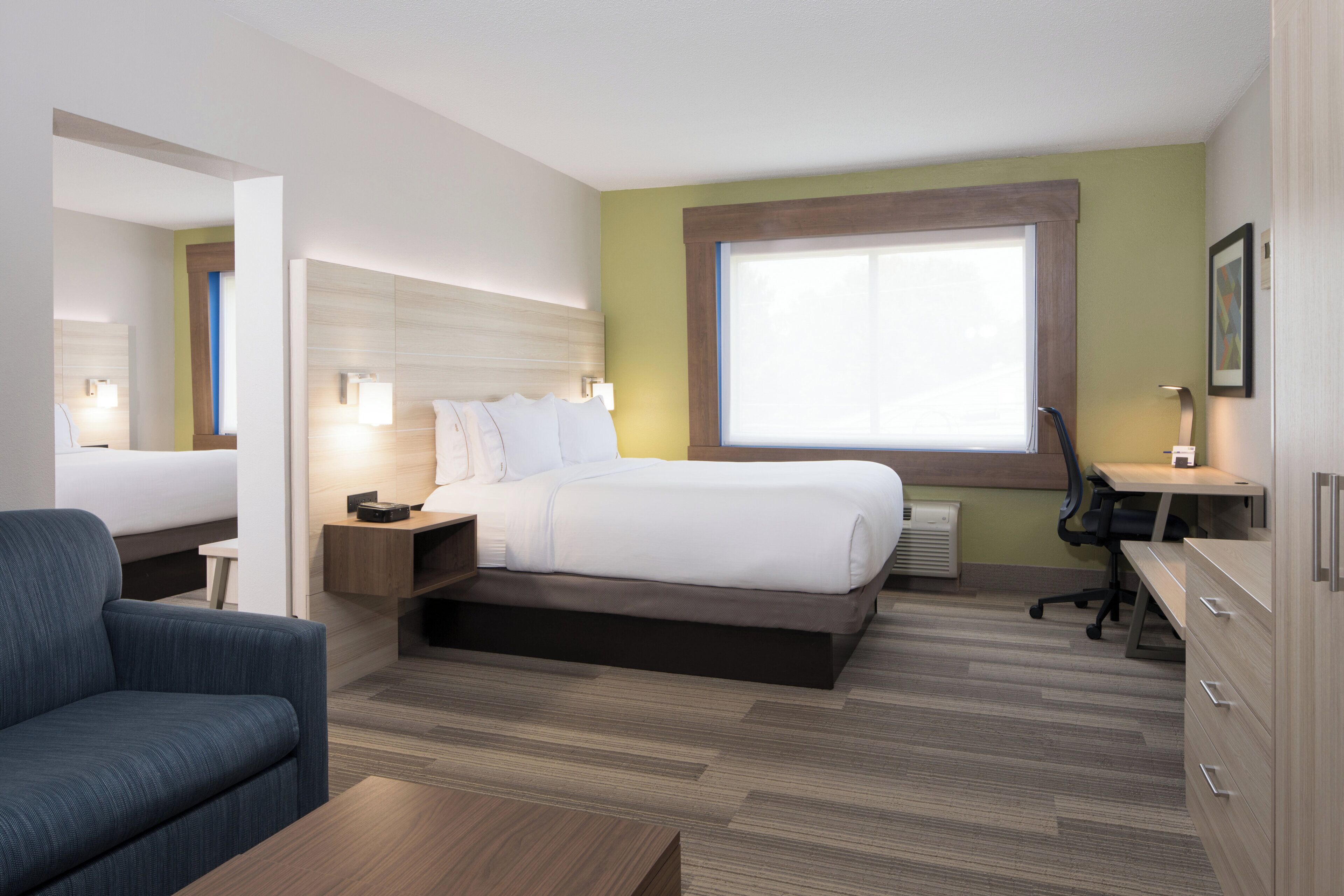 A hotel room with a bed, bedside tables, a desk, a chair, and a large window.