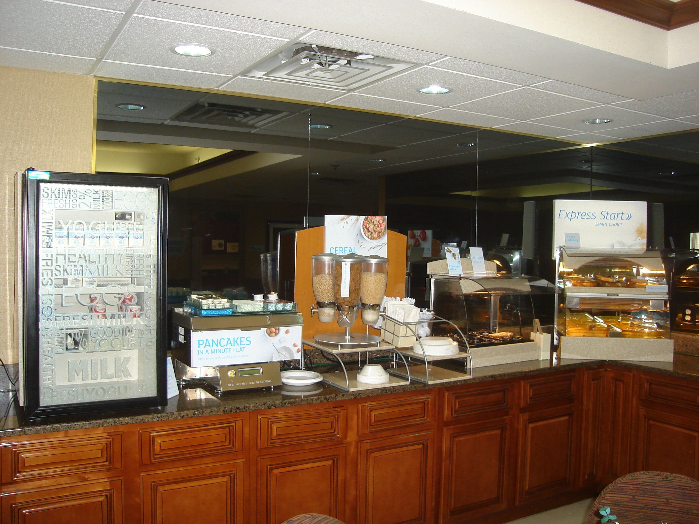 A breakfast bar with a refrigerator displaying fresh ingredients, a cereal dispenser, and a sign for 'Express Start' breakfast.