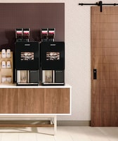 Una estación de café moderna con dos máquinas de espresso, un dispensador de café y una encimera de madera.
