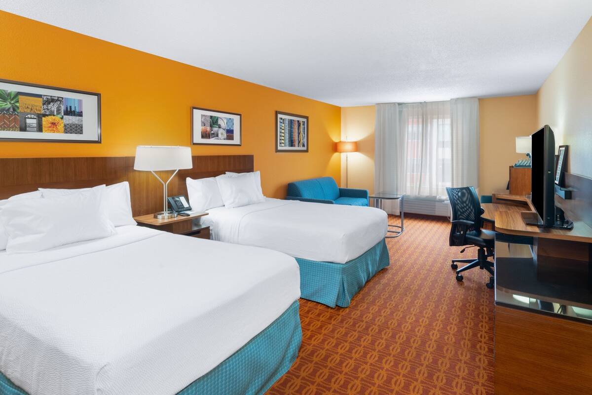 A hotel room with two beds, a desk, a chair, and a TV.