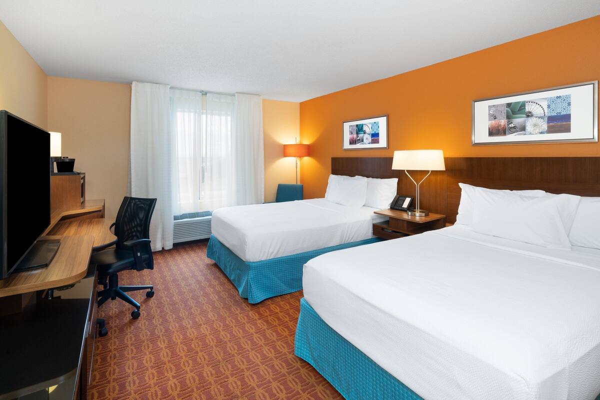 A hotel room with two beds, a desk with a computer, a chair, and two lamps.