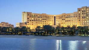 A large hotel with multiple floors and balconies, a beach in the foreground, and palm trees. - InterContinental Doha Beach & Spa by IHG (Doha)