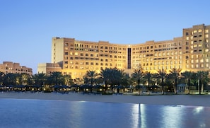 A large hotel with multiple floors and balconies, a beach in the foreground, and palm trees. - InterContinental Doha Beach & Spa by IHG (Doha)