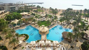 A resort with a central swimming pool, palm trees, and a beach area.
