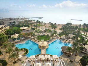 A resort with a central swimming pool, palm trees, and a beach area.