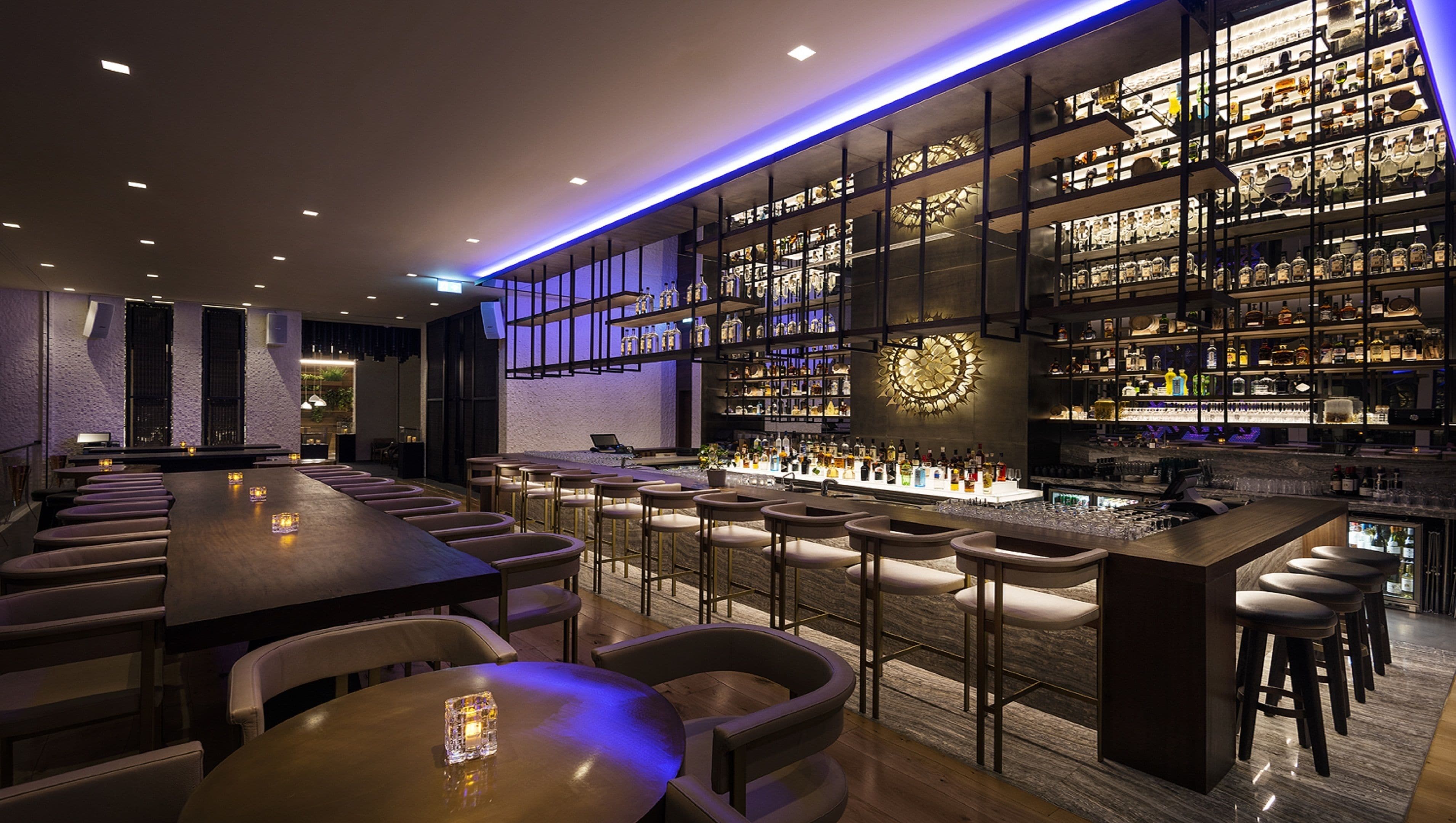 Una zona de bar con una barra larga, varios taburetes y estantes llenos de botellas.