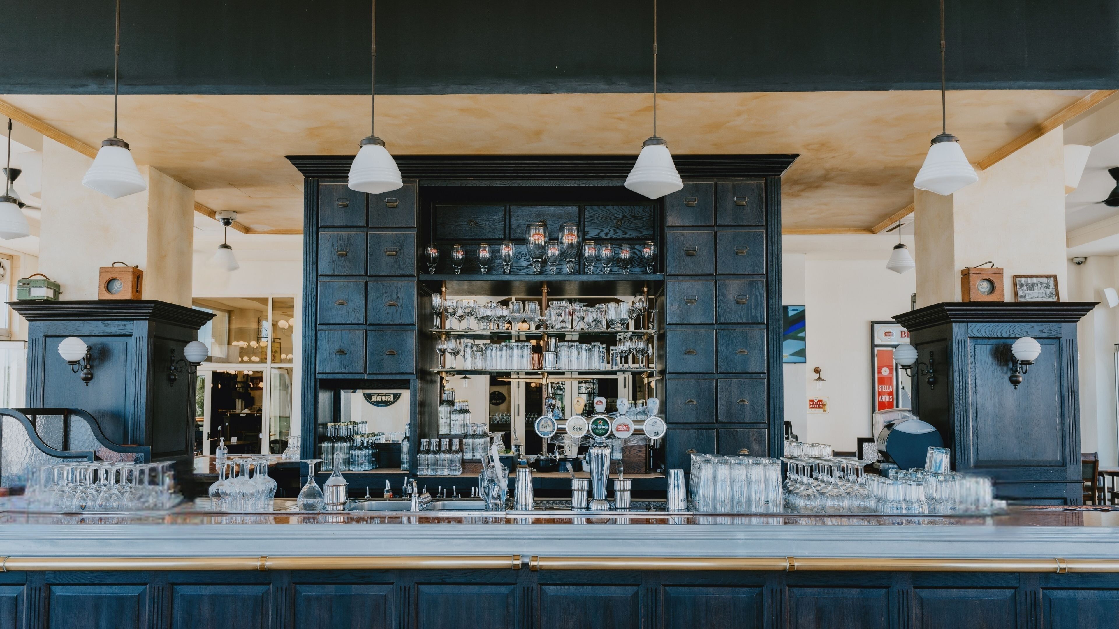 A bar area with a counter, shelves of glassware, and hanging pendant lights.