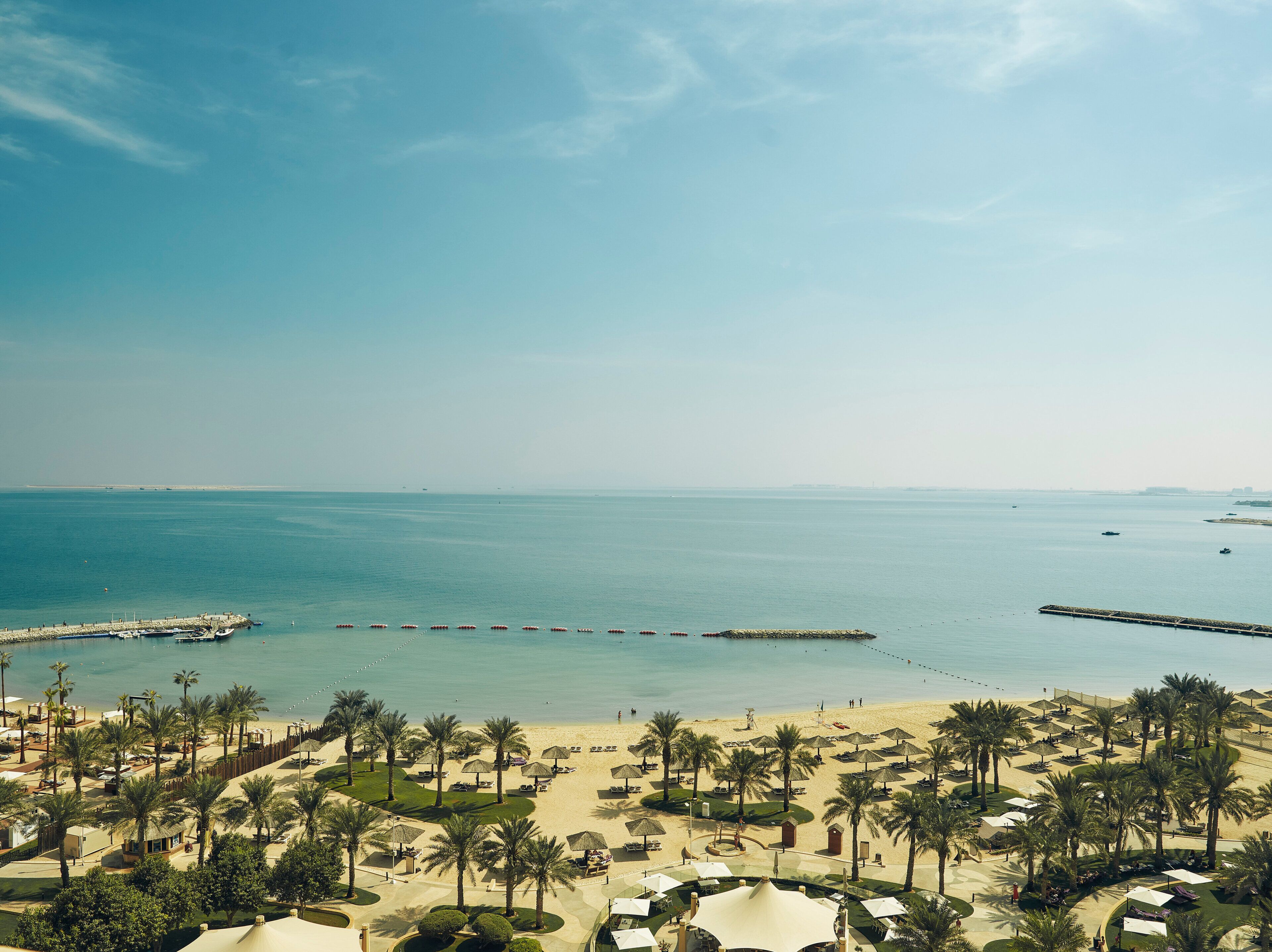 Un resort en la playa con palmeras, sillas de descanso y un muelle que se adentra en el mar.