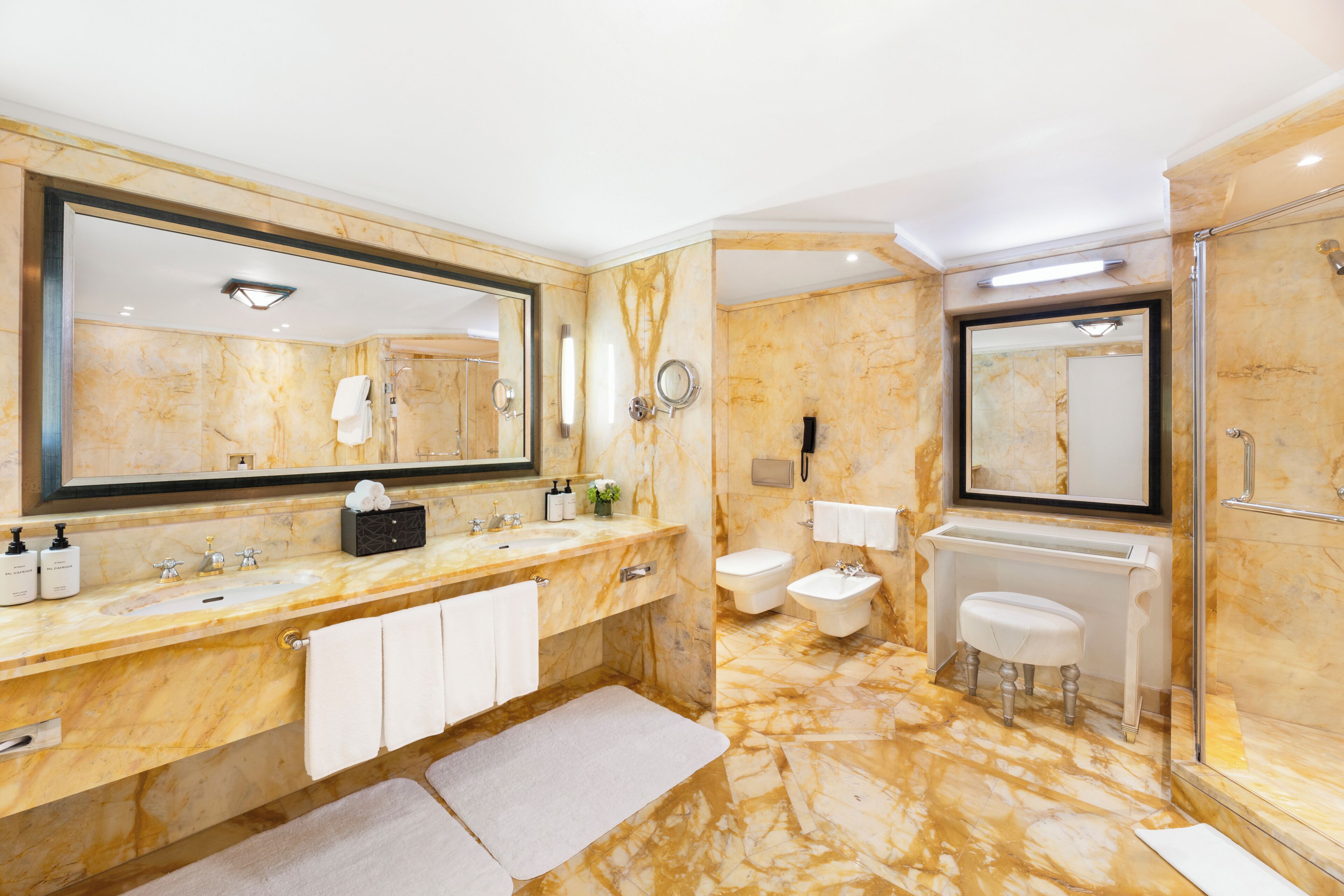 A bathroom with a marble floor, a large mirror, a sink, a toilet, and a shower area.
