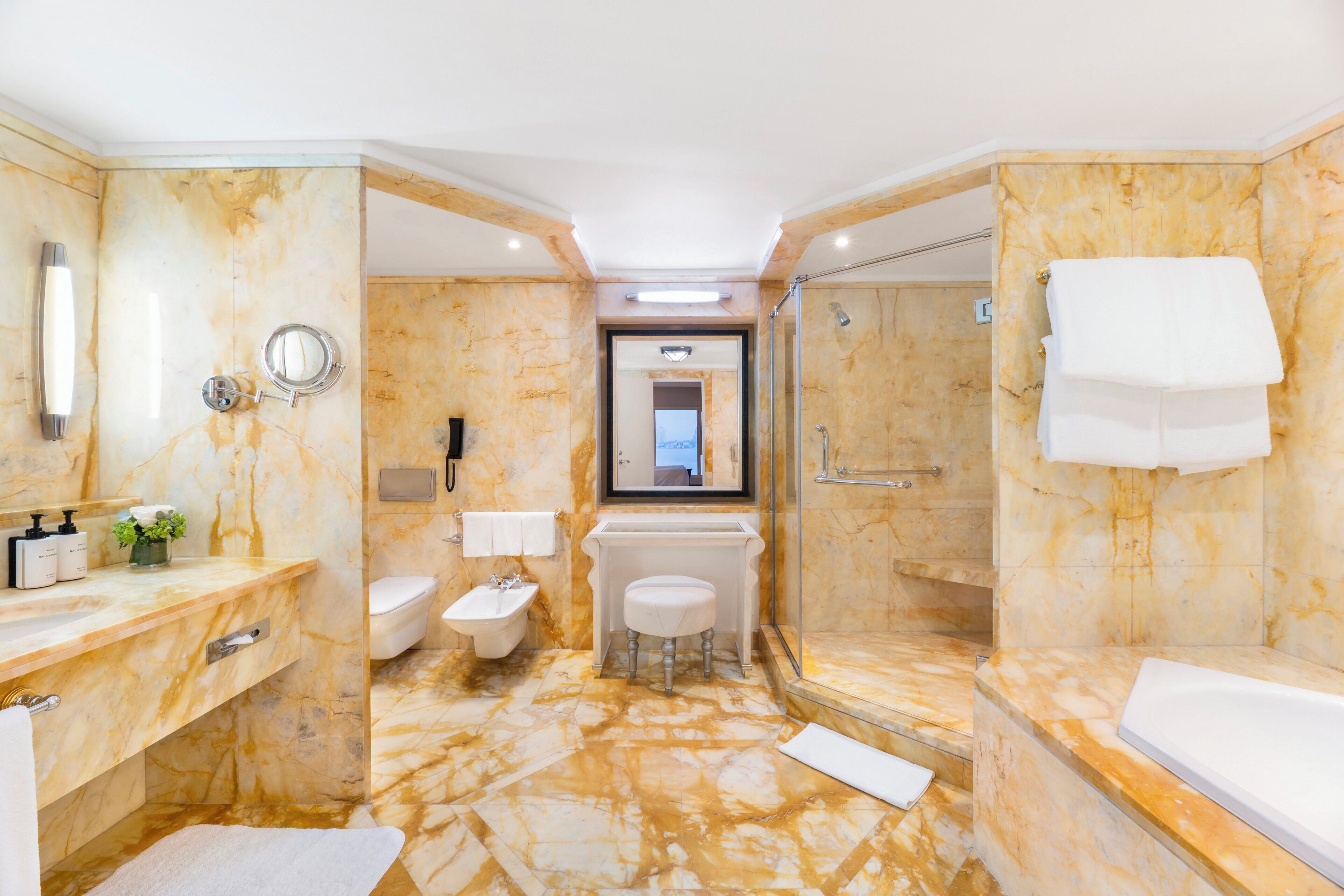 Un baño con piso de mármol, un lavamanos, un inodoro, un bidé, un espejo y una ducha.