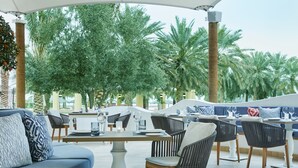 An outdoor seating area with tables and chairs, surrounded by palm trees and greenery.