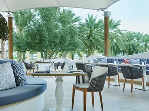 An outdoor seating area with tables and chairs, surrounded by palm trees and greenery.