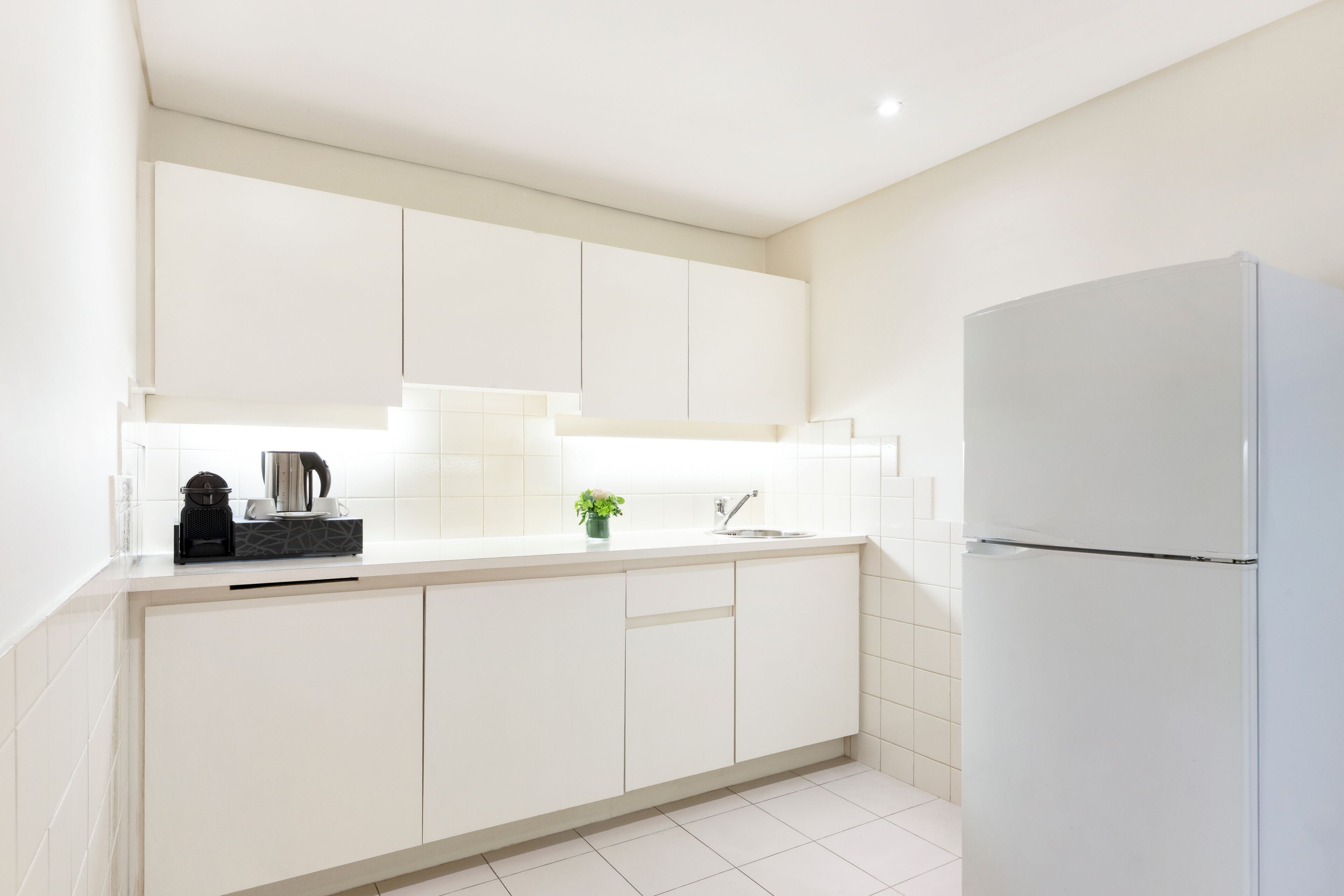 A modern kitchen with white cabinets, a stainless steel refrigerator, and a coffee maker on the counter.