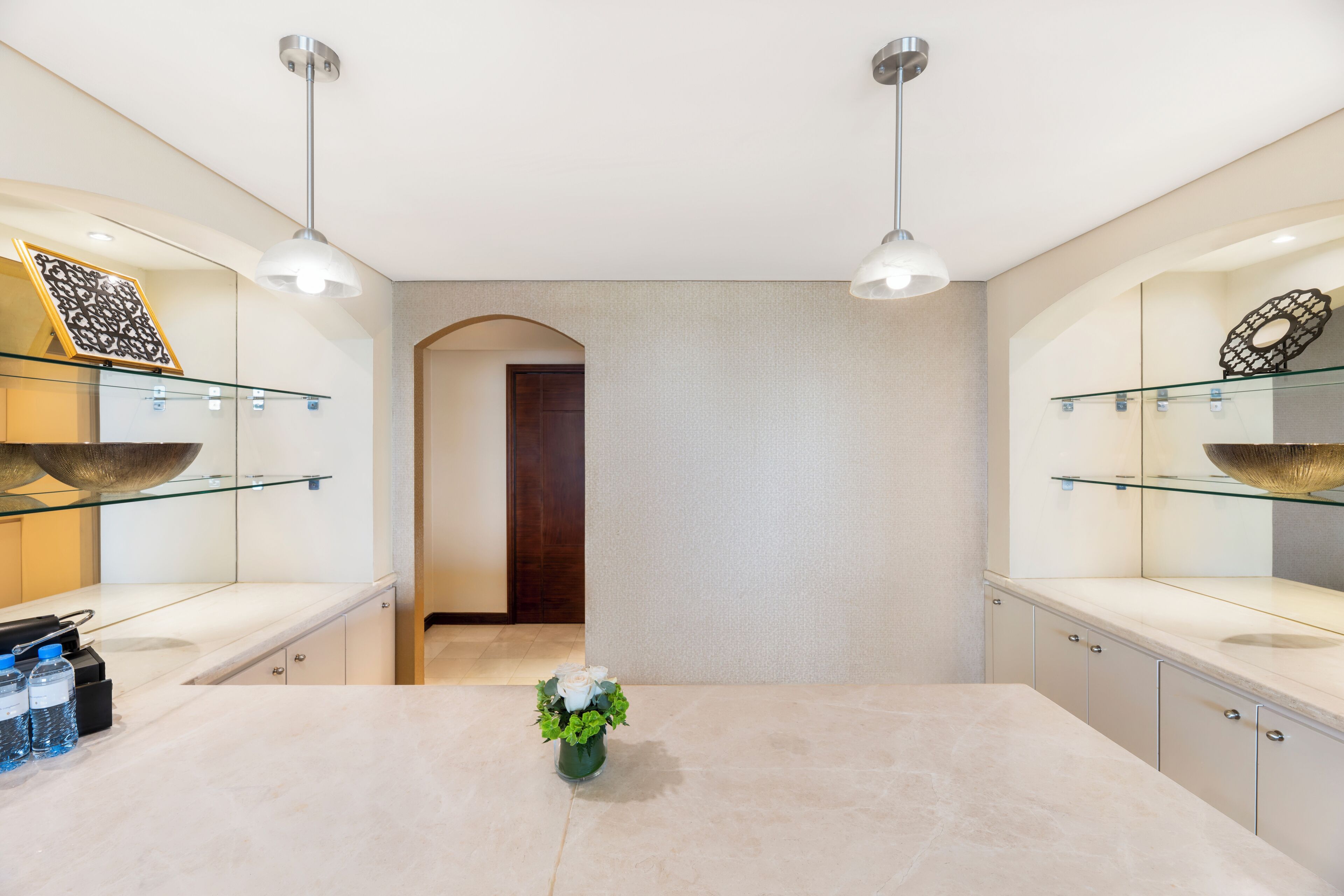 A modern kitchen with a marble countertop, two pendant lights, and a vase with flowers.