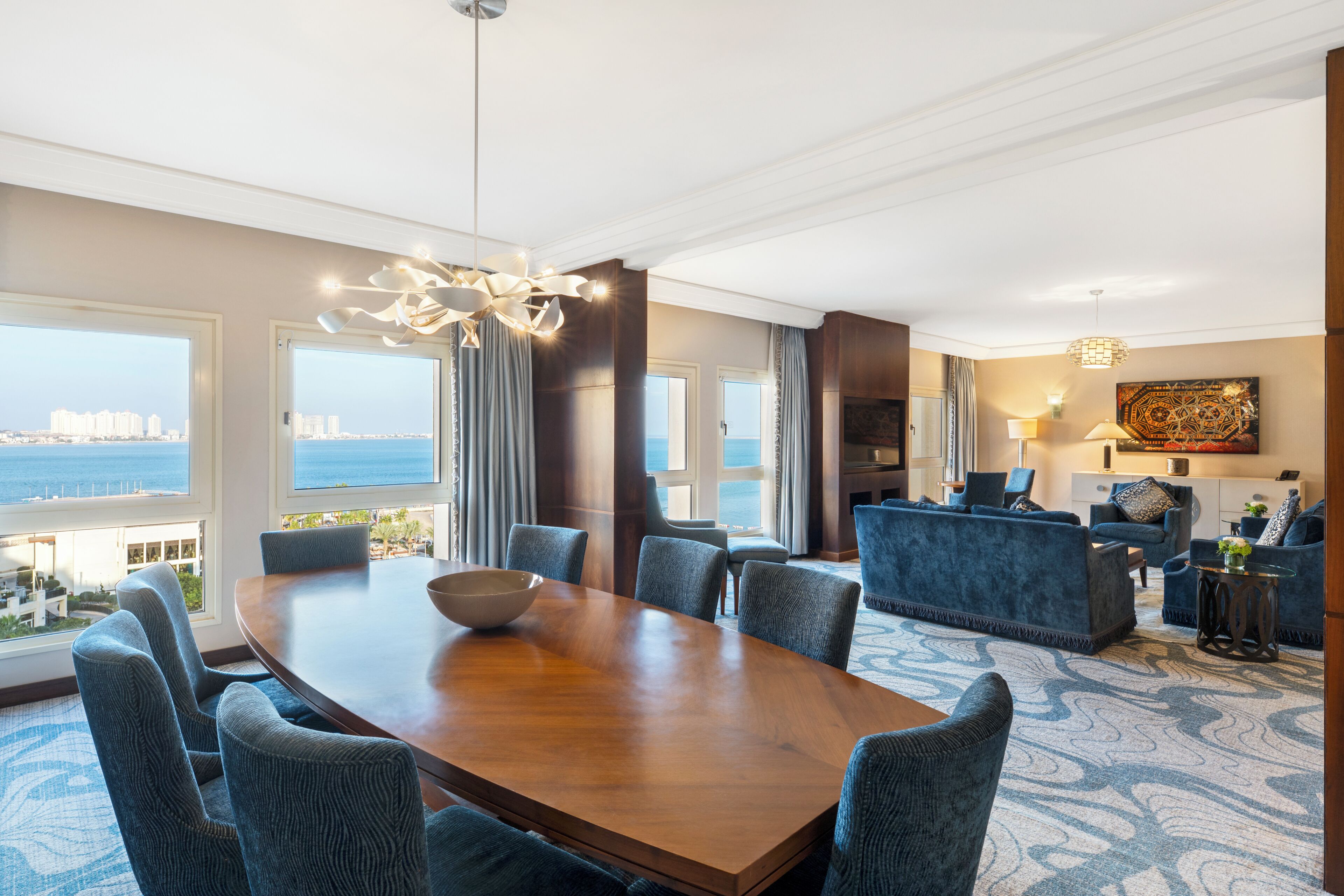 A hotel room with a dining area, a living area with a sofa, a view of the city, and a large window.