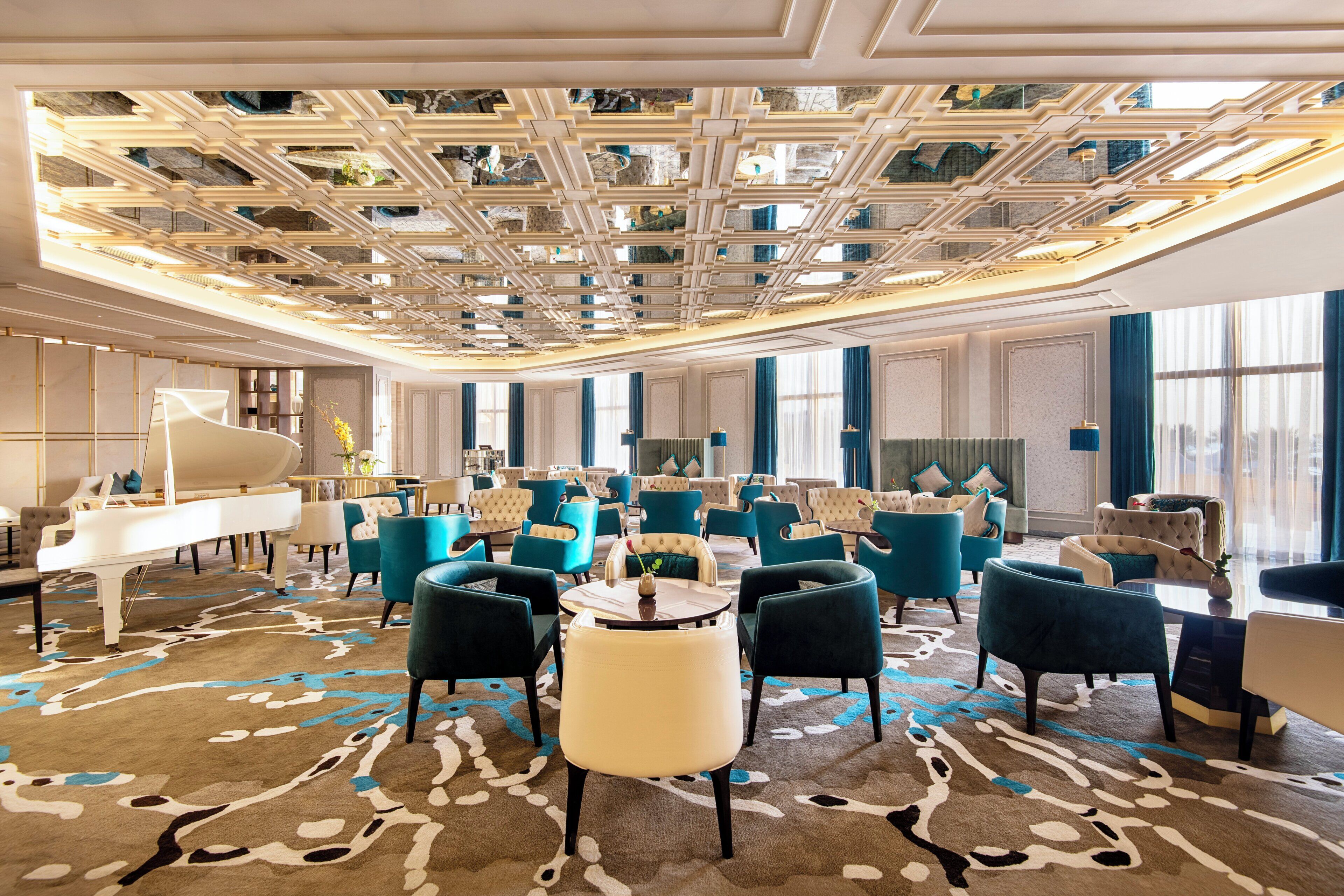 A spacious hotel lobby with a grand piano, multiple seating areas, and a patterned carpet.