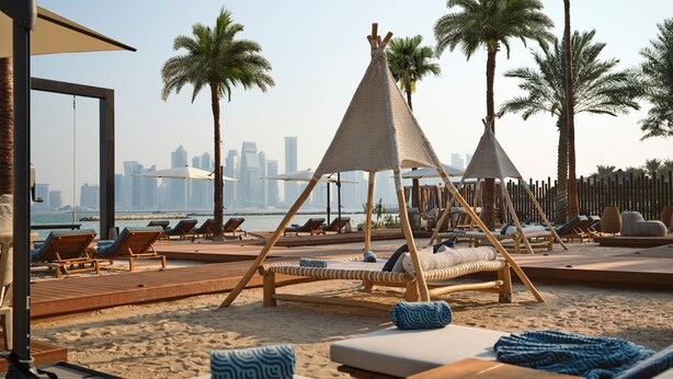 A beachside resort with lounge chairs, wooden deck, and a city skyline view. - InterContinental Doha Beach & Spa by IHG (Doha)