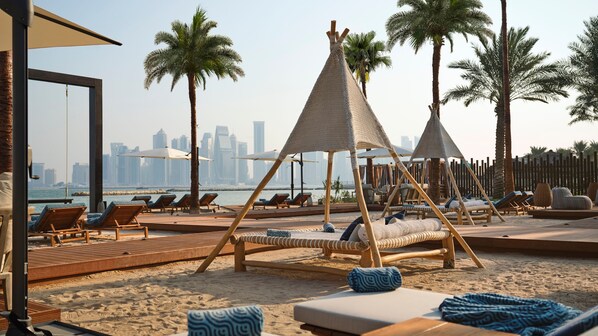 A beachside resort with lounge chairs, wooden deck, and a city skyline view.