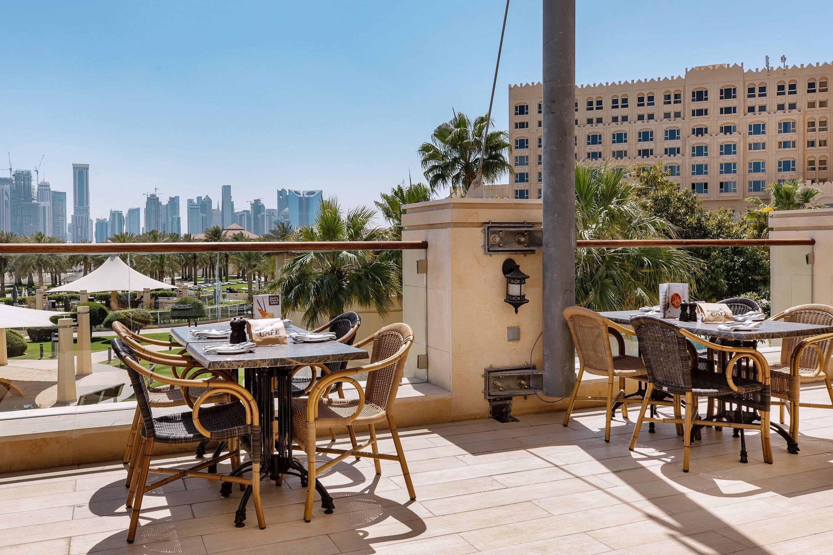 Un espace de restauration en plein air, avec des chaises et des tables en osier, offrant une vue sur les toits de la ville et ses bâtiments modernes.