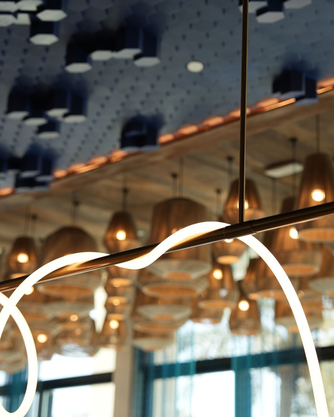 Un plafond orné de plusieurs luminaires suspendus et dont on peut voir la structure en poutres métalliques.