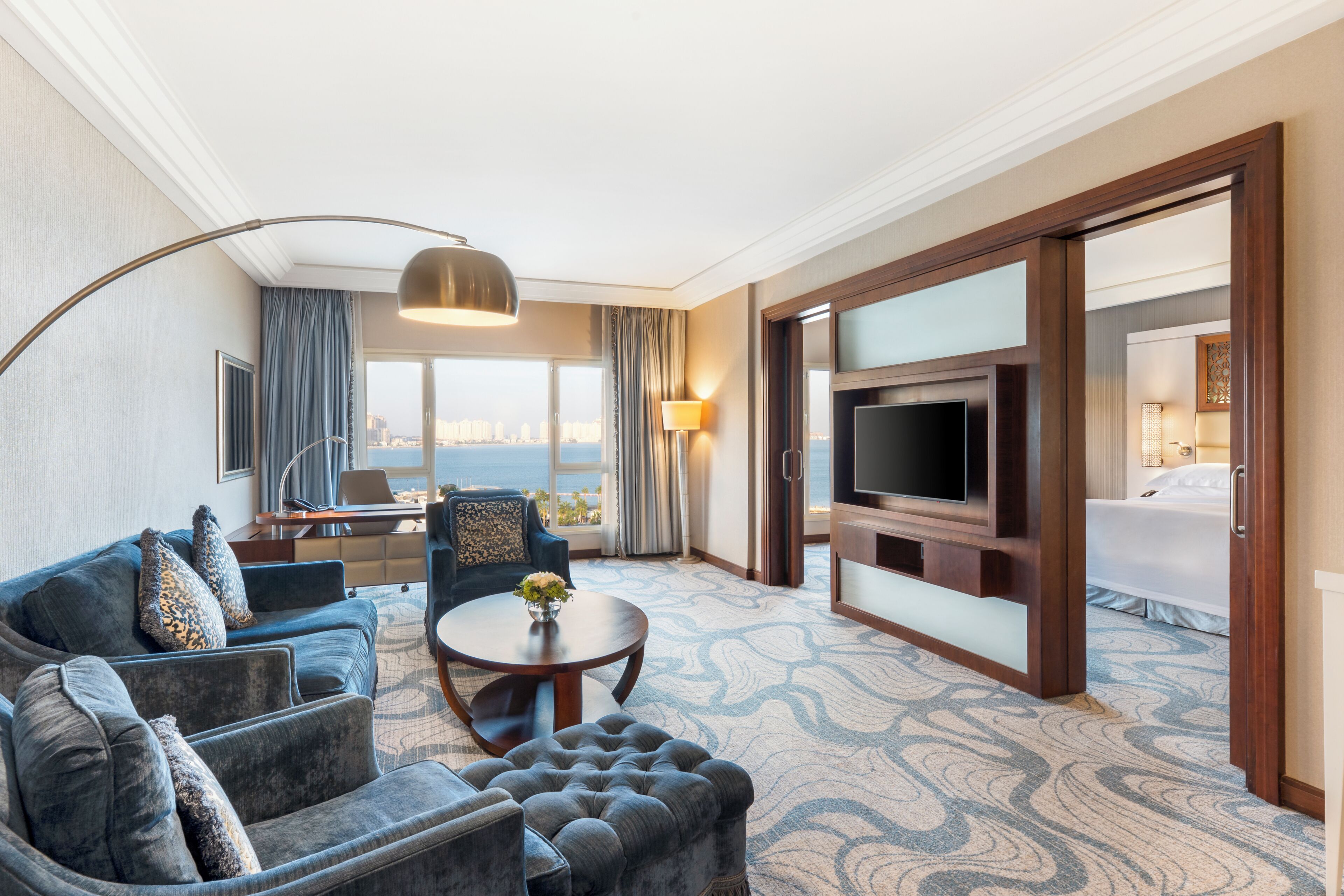 Hotelkamer met een bank, fauteuil, ronde tafel, televisie en uitzicht op de stad.