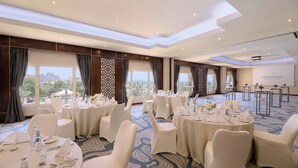 A conference room with round tables, white chairs, and a city view. - InterContinental Doha Beach & Spa by IHG (Doha)