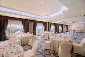 Una sala conferenze con tavoli rotondi, sedie bianche e vista sulla città.
