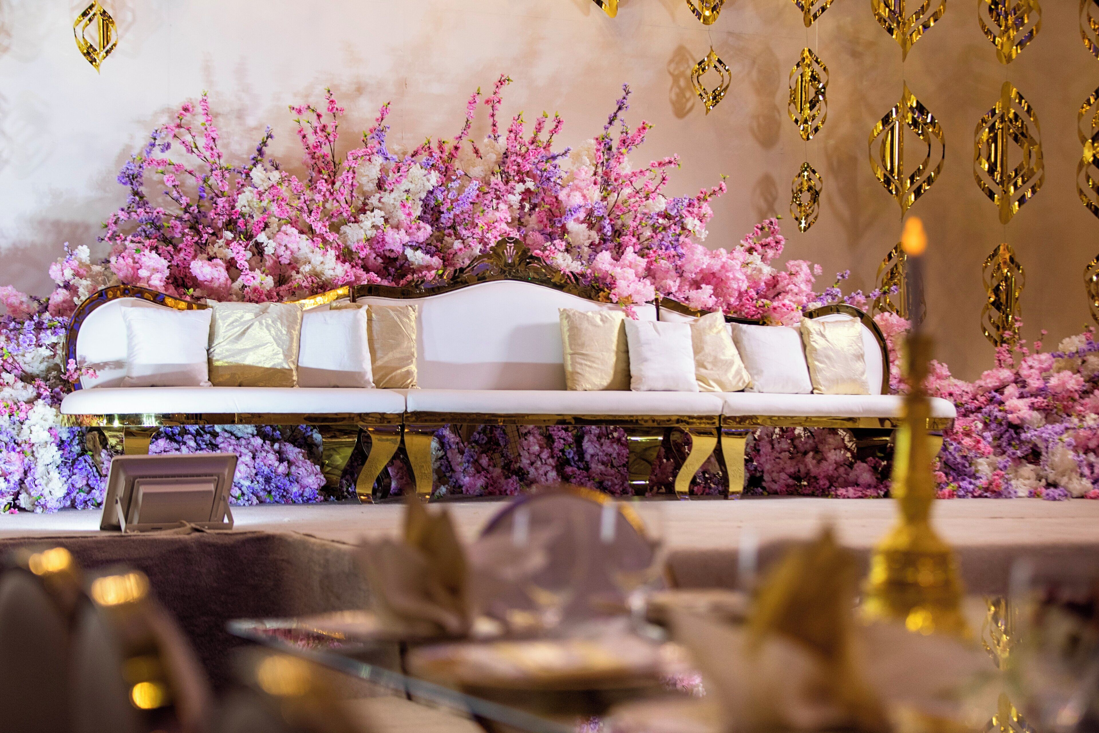 A sofa with multiple cushions, a floral arrangement, and a reflective gold base.