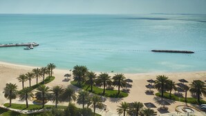 A beach resort with palm trees, beach umbrellas, and a pier extending into the sea. - InterContinental Doha Beach & Spa by IHG (Doha)