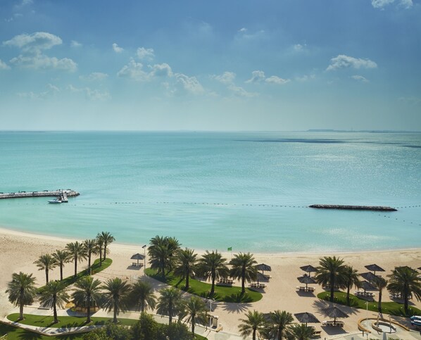 Un resort sulla spiaggia con palme, ombrelloni e un molo che si protende verso il mare.