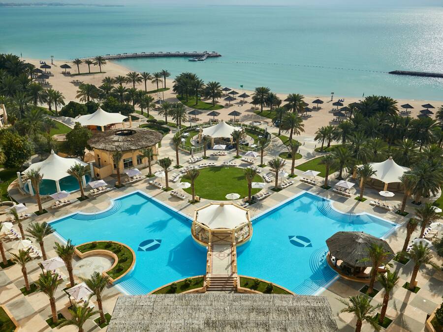 Ein Resort mit einem zentralen Schwimmbad, Zugang zum Strand und Palmen.