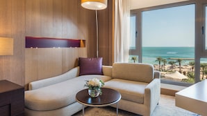 A modern hotel room with a large window offering a view of the beach, a sofa, a small table with a vase of flowers, and a pendant light. - InterContinental Doha Beach & Spa by IHG (Doha)
