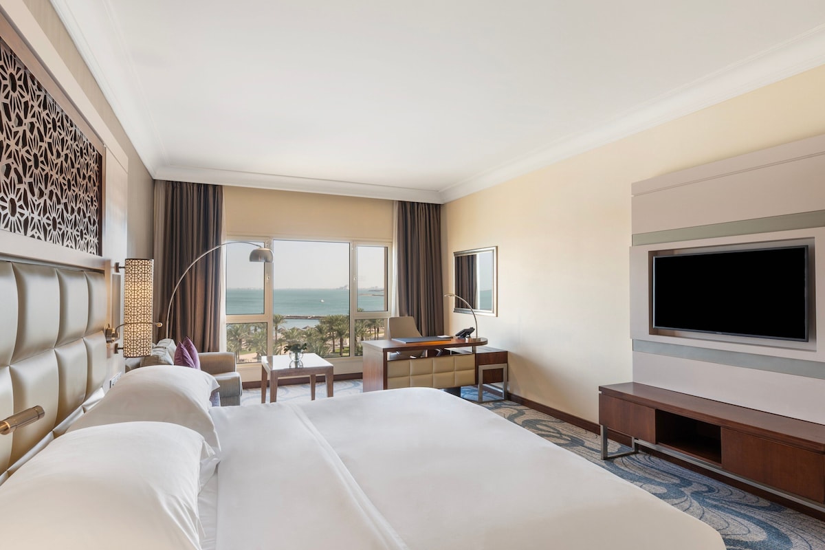 A hotel room with a large bed, a desk, a TV, and a view of the ocean.