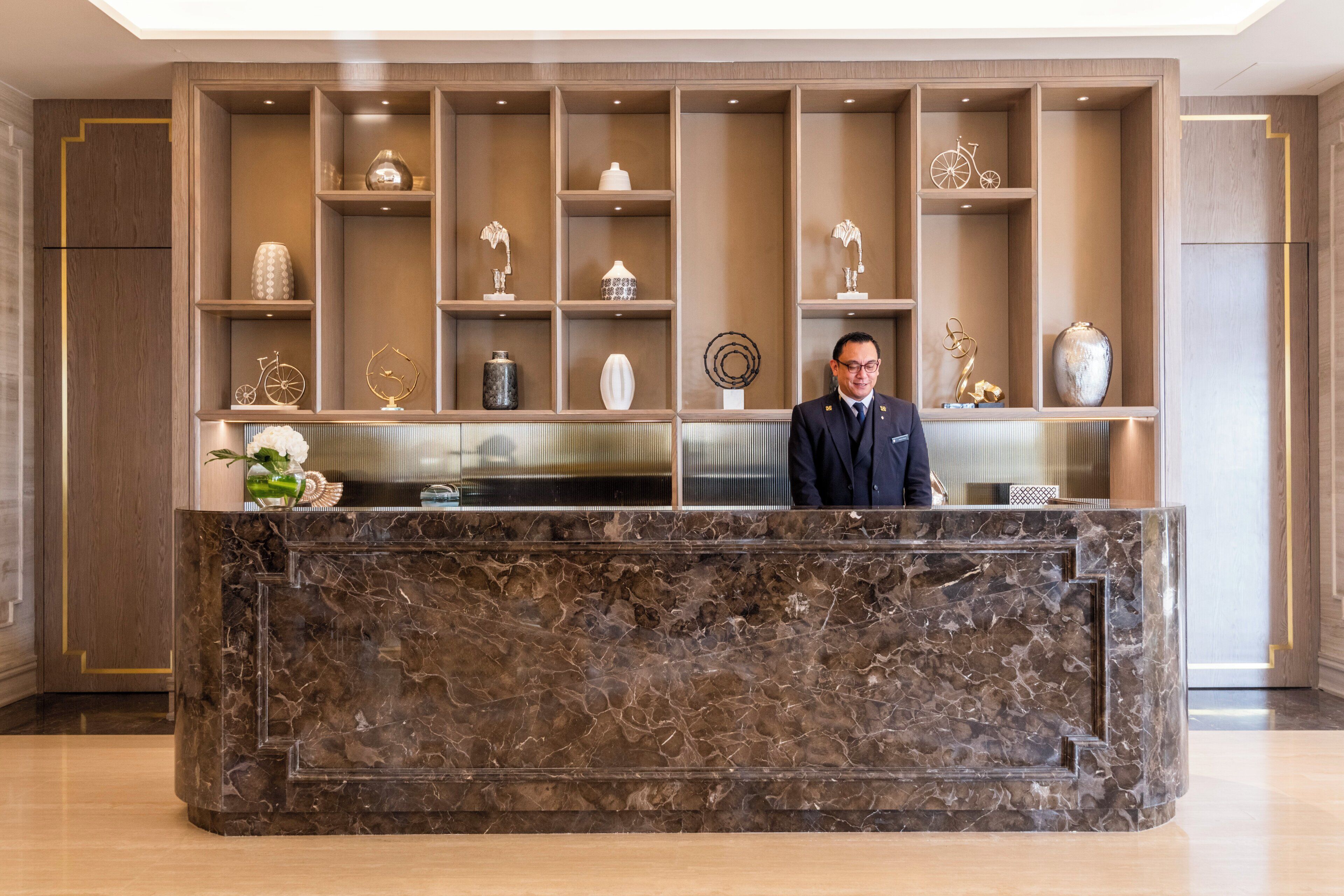 A reception desk with a marble top, flanked by wooden shelving with various decorative items.