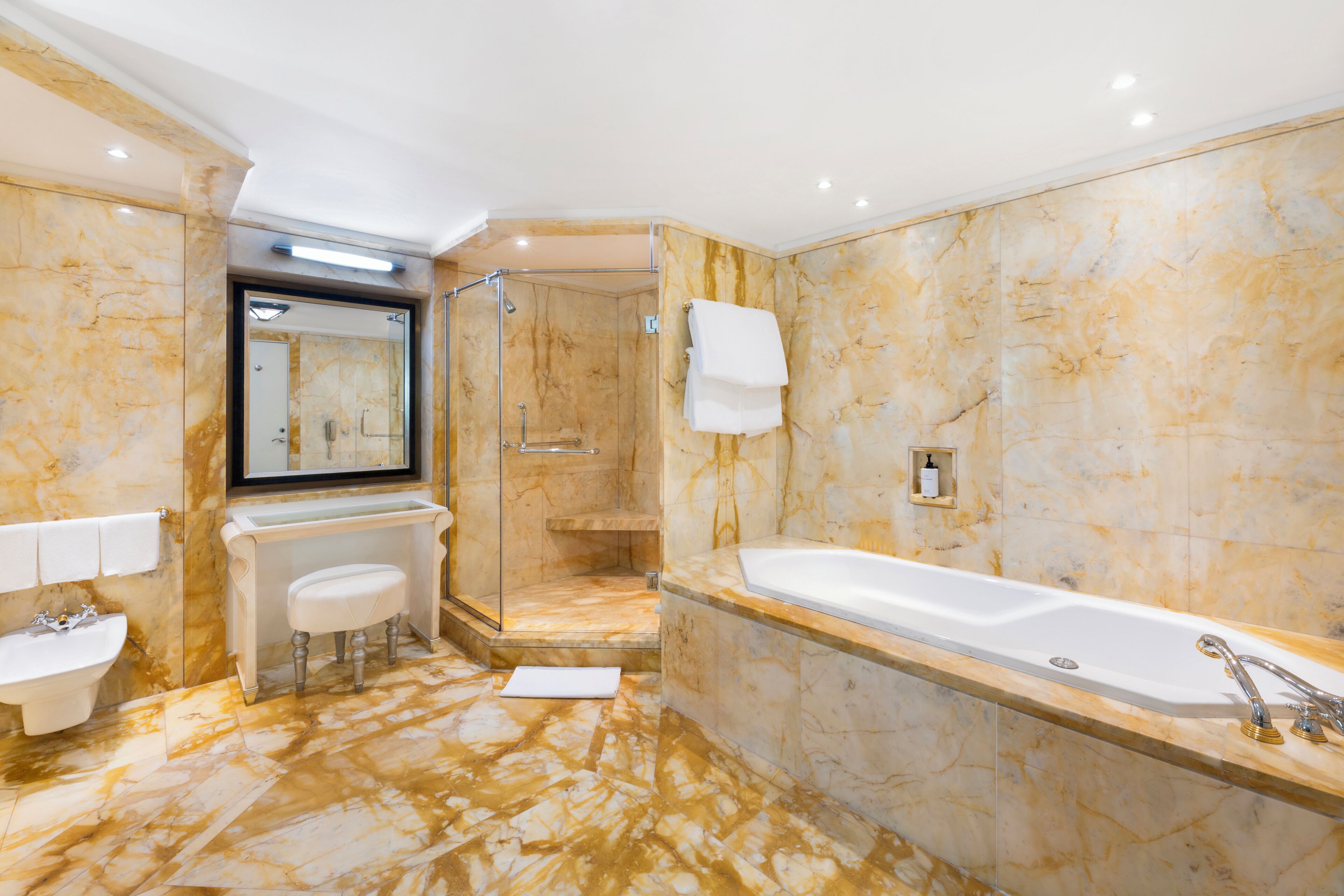 A modern bathroom with a bathtub, a sink, a shower, and marble walls.