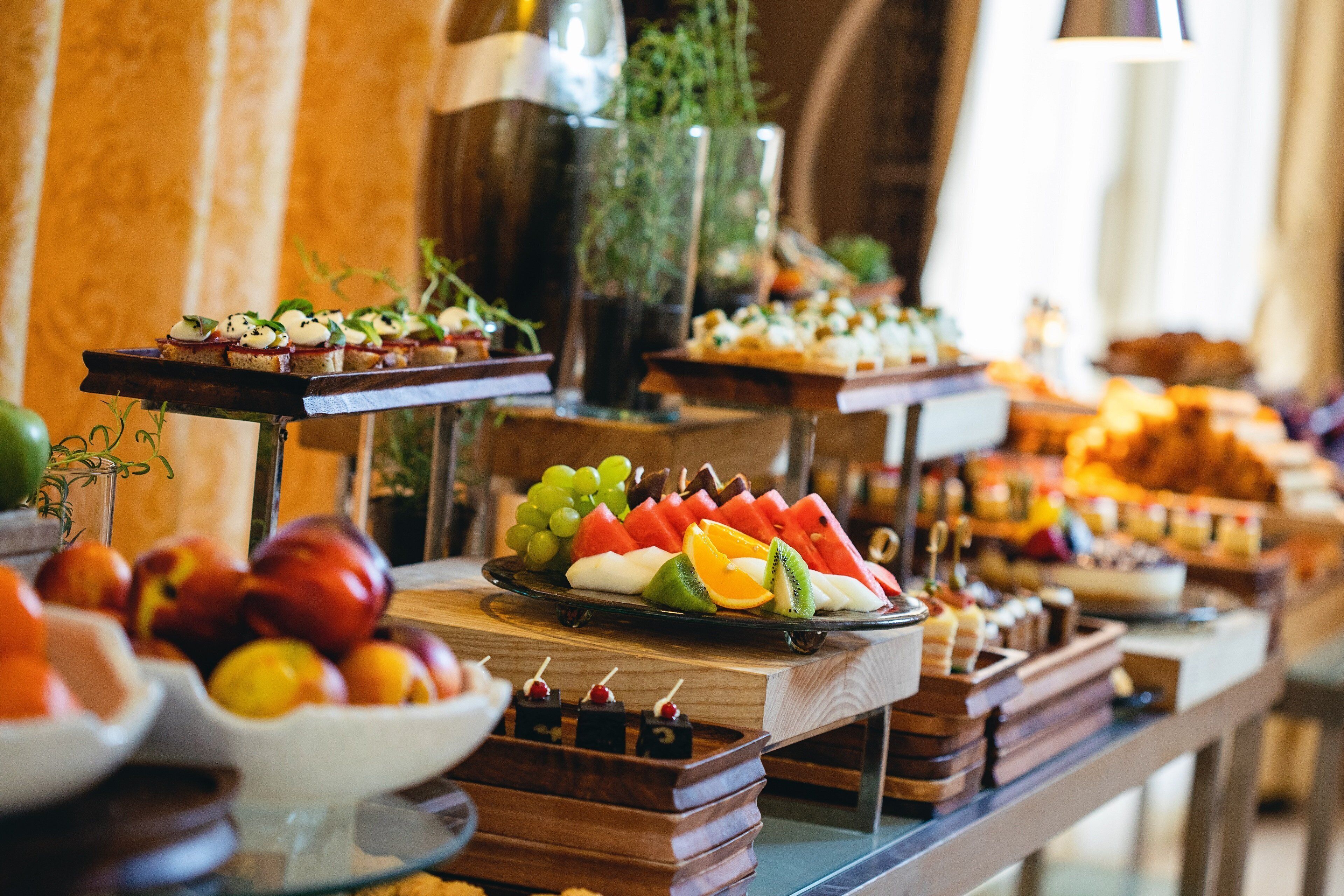 Un bufé con diversas opciones de comida, entre ellas frutas, quesos y aperitivos.