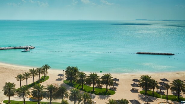 A beach resort with a clear view of the ocean, a pier, and palm trees.