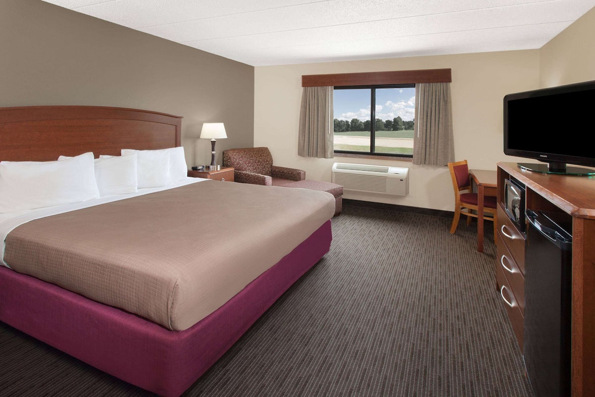 Ein Hotelzimmer mit einem großen Bett, einem Schreibtisch mit Fernseher, einem Sessel und einem Fenster mit Blick auf einen Golfplatz.
