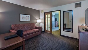 Une chambre d’hôtel équipée d’un canapé, d’un bureau, d’une lampe, d’un miroir et d’une porte donnant sur une autre pièce.