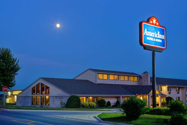 A motel with a prominent sign, a stop sign, and a well-lit building at dusk. - AmericInn by Wyndham Grundy Center (Grundy Center)
