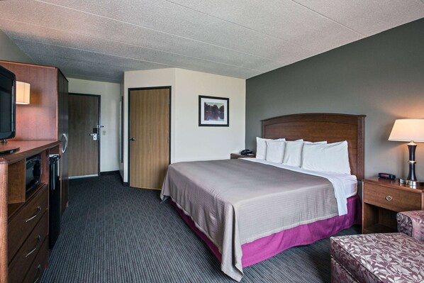 A hotel room with a large bed, a desk, a chair, a television, and a door.