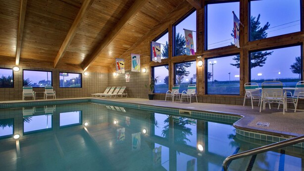 Une piscine intérieure dotée de poutres en bois au plafond, de grandes fenêtres et de chaises longues.