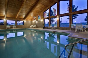 An indoor swimming pool with wooden ceiling beams, large windows, and lounge chairs. - AmericInn by Wyndham Grundy Center (Grundy Center)