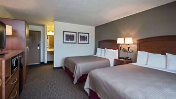 A hotel room with two beds, a desk, a dresser, and a television.