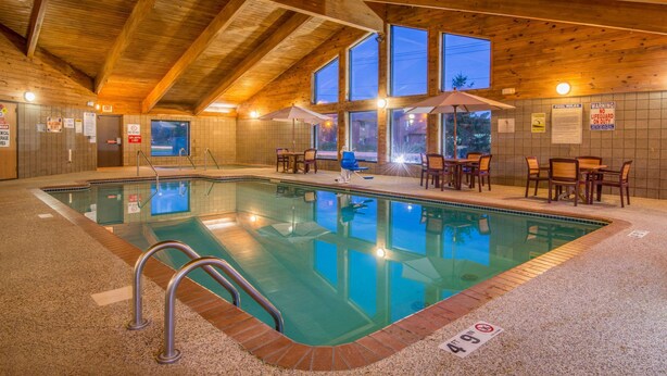 An indoor swimming pool with wooden beams, tiled walls, and a seating area with tables and chairs. - AmericInn by Wyndham Ames (Ames)