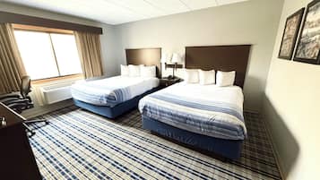 Une chambre d’hôtel avec deux lits, un bureau, une chaise, une fenêtre avec des rideaux et un tapis à motifs.