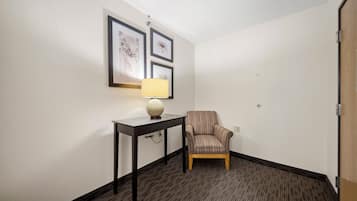 Una habitación de hotel con una sola silla, una mesita con lámpara y obras de arte enmarcadas en la pared.