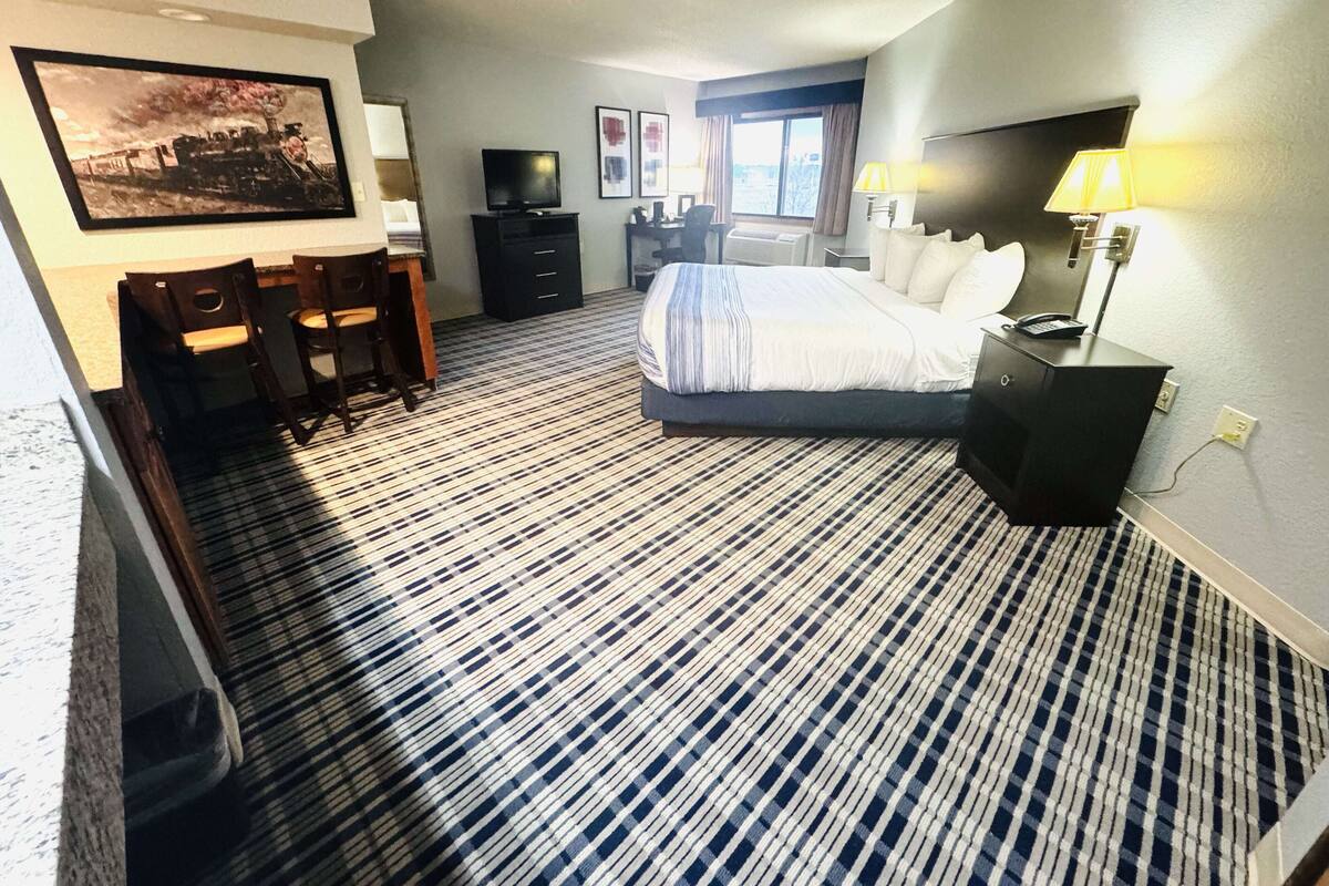 A hotel room with a bed, desk, chair, television, and artwork on the walls.