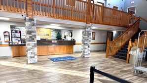 A spacious lobby with a reception desk, a wooden staircase, and a blue mat with "American Inn" text. - AmericInn by Wyndham Ames (Ames)